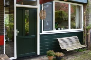 Nieuwe kunststof deur, gevelbekleding en kozijnen geplaatst in de kleur groen. Gemaakt in een voortuin.